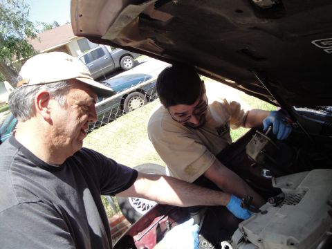 1995 Ford Taurus - Two men are working on the engine of a car, with other vehicles visible in the background.