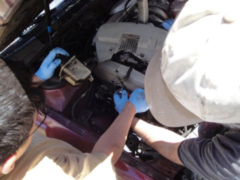 1995 Ford Taurus - Two individuals are actively working on the engine of a maroon vehicle, with the hood open.