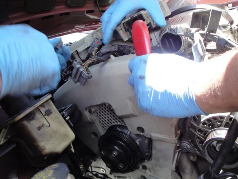 1995 Ford Taurus - Mechanics work on engine components, including a pulley and hoses, in a vehicle's engine bay.