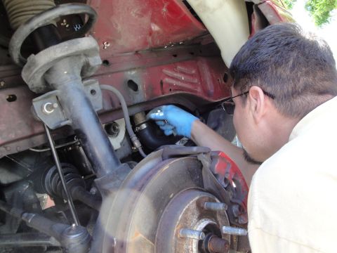 1995 Ford Taurus - Close-up of a mechanic's hands working on a vehicle's engine bay, focusing on a hose clamp and suspension components.