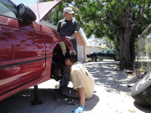 1995 Ford Taurus - Mechanics work on a 1995 Ford Taurus, with another vehicle visible in the background.