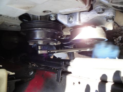 1995 Ford Taurus - Close-up view of an engine belt tensioner pulley being worked on with a socket wrench.