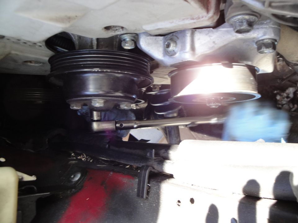 Engine belt tensioner pulley with a socket wrench. Blue glove visible