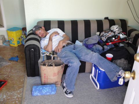 1995 Ford Taurus - A man sleeps on a striped couch, surrounded by various items including a grocery bag and a blue cooler.
