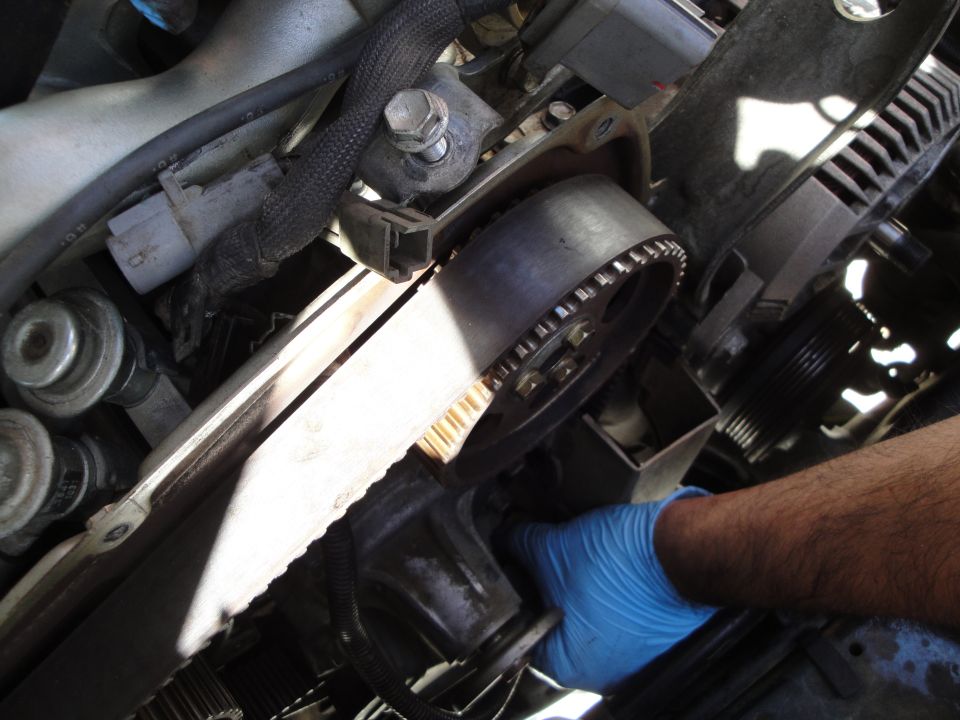 Engine timing belt and pulley system with a gloved hand reaching into the mechanism