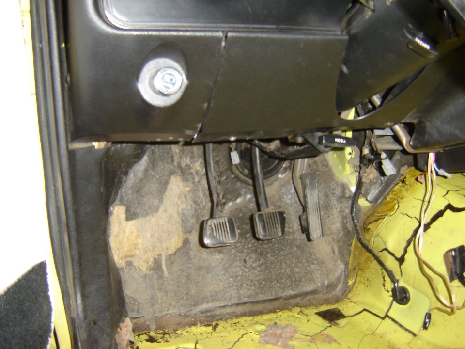 Car interior footwell showing clutch, brake, and accelerator pedals. Yellow floor and black dashboard visible