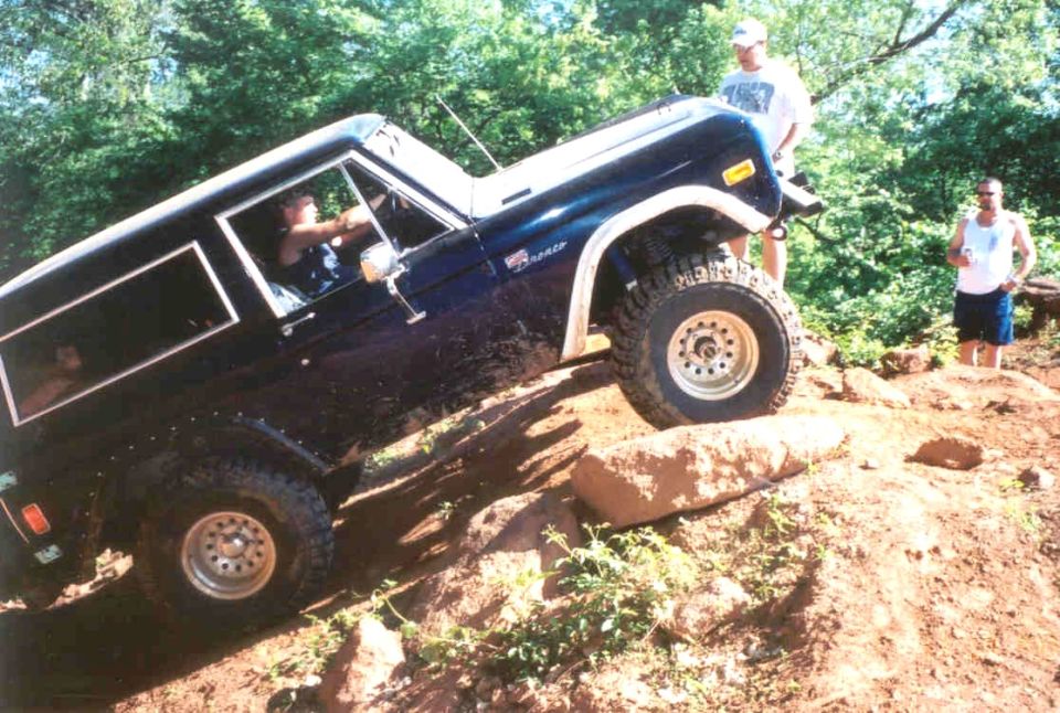 Dark blue lifted Ford Bronco on big off-road tires climbing a steep rocky ledge on a trail