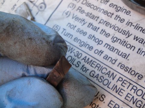 1995 Ford Taurus - A close-up shows gloved hands holding a small metal piece over a document detailing American petroleum oils for gasoline engines.