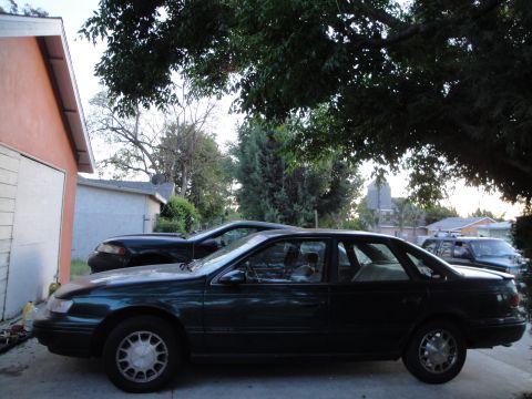 1995 Ford Taurus - A dark green sedan is parked in front of a garage, with another car visible behind it.
