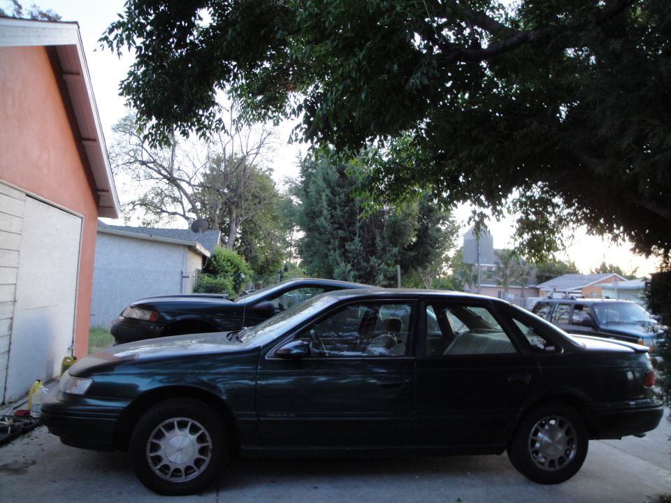 dark green sedan parked next to a black car in a driveway