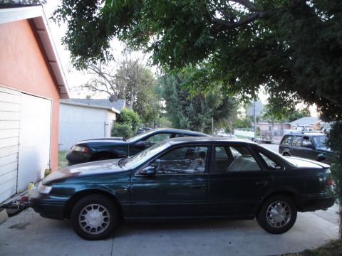 1995 Ford Taurus - A dark green sedan, likely a 1992 Ford Taurus, is parked in a driveway next to a garage.