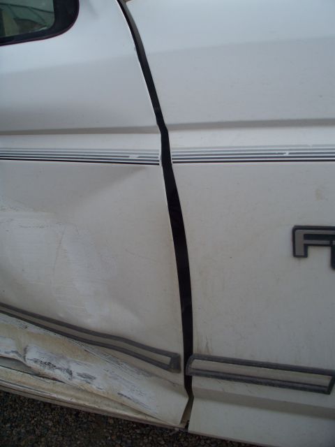 1992 Ford F-250 - The side panel of a white 1992 Ford F-250 shows significant damage and a gap between doors.