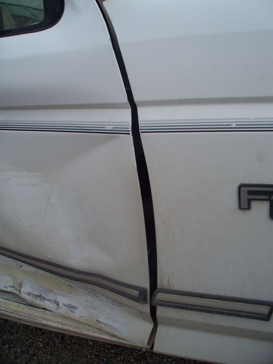Side view of a damaged white 1992 Ford F-250 door with trim and dented lower panel