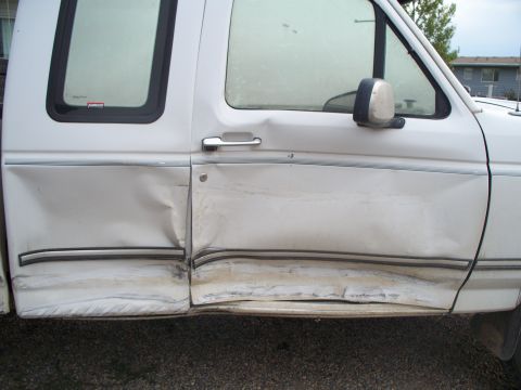 1992 Ford F-250 - Driver's side door and fender of a white 1992 Ford F-250 show significant collision damage.