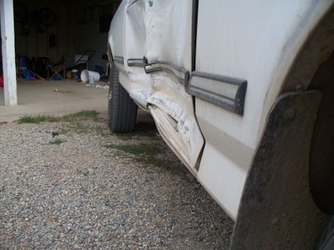 1992 Ford F-250 - The side of a white truck shows extensive damage to the door and lower body panels, with visible rust and repair work.