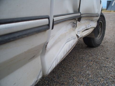 1992 Ford F-250 - The side of a white truck shows extensive damage, including a crumpled lower body panel and dented door.