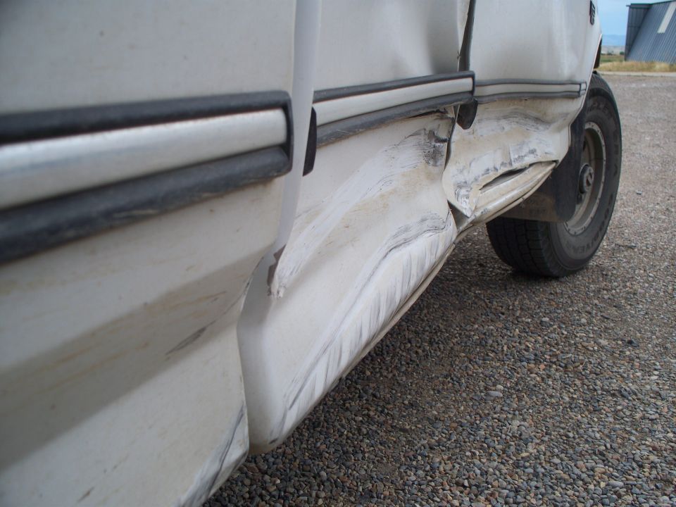 White truck side with significant damage to the lower body and door panel