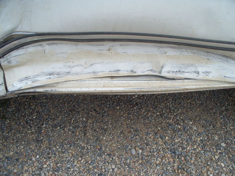 close-up of dented white vehicle body panel with black trim above it