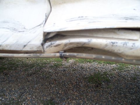 1992 Ford F-250 - Close-up of a damaged white vehicle body panel, showing bent metal and a zip tie.