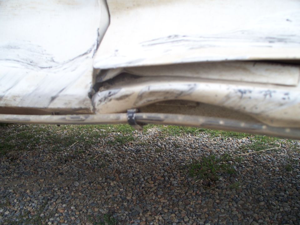 White vehicle body panel with significant damage and a black zip tie securing a metal rod