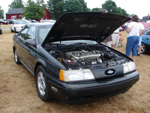 1992 Ford Taurus - A black 1992 Ford Taurus SHO is displayed with its hood open, revealing the V8 engine, at an outdoor car event.