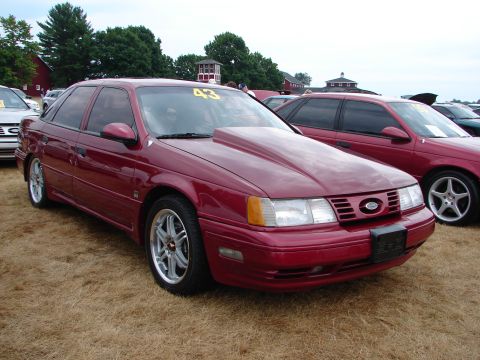 1992 Ford Taurus - A modified 1992 Ford Taurus with a prominent hood scoop and custom wheels at a car show.