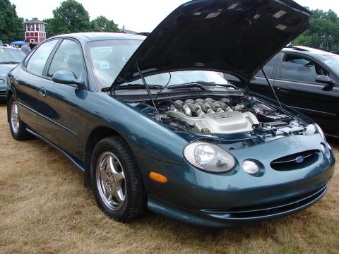1992 Ford Taurus - A teal sedan with its hood open, revealing a V8 engine, parked on grass next to another car.