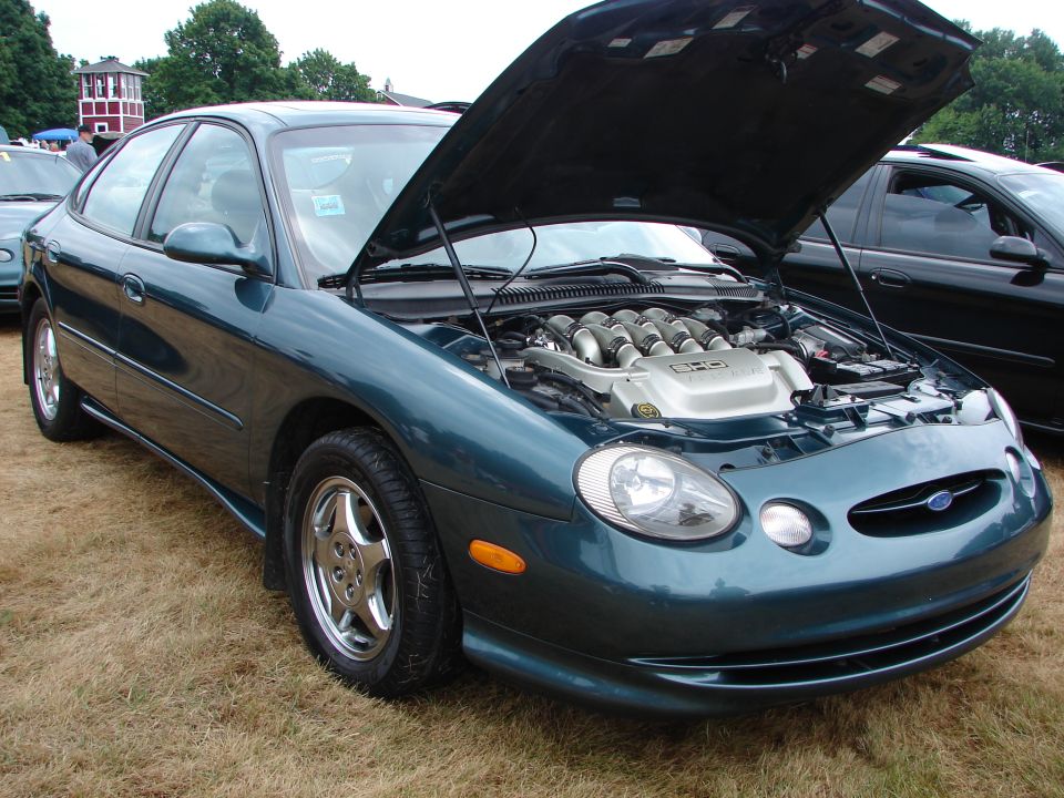 Teal sedan with hood open, showing V8 engine. Chrome wheels, slight damage on front bumper