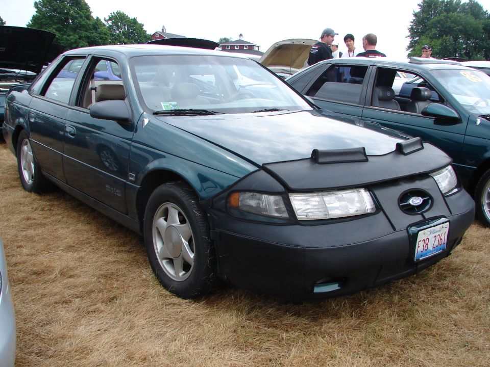 Green 1992 Ford Taurus with a black car bra parked on grass, another Taurus behind it