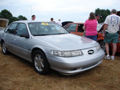 1992 Ford Taurus - A silver sedan with a yellow '82' sticker on the windshield is parked on grass at an outdoor event.