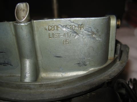 1968 Shelby GT500 - A metal carburetor part is shown with stamped identification numbers.