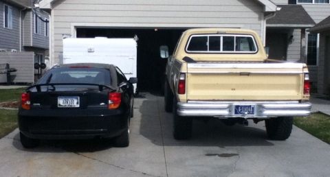 2006 Ford E350 - A black Toyota Celica is parked next to a tan pickup truck in front of a garage.