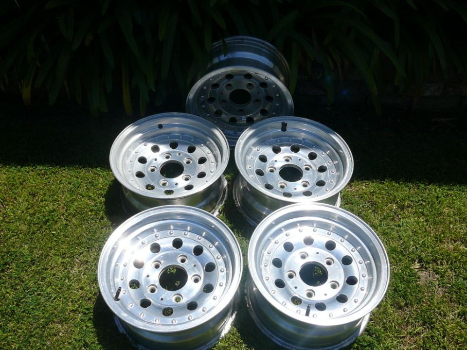 Five polished aluminum 5-lug wheels with round-hole spokes arranged on grass