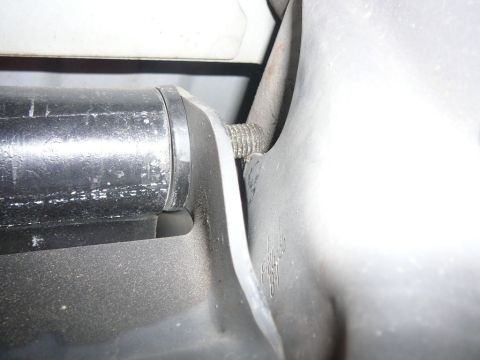 1988 Ford Bronco - Extreme close-up of a dusty black plastic and stamped-steel bracket under a vehicle, showing an exposed threaded stud passing through a slo…