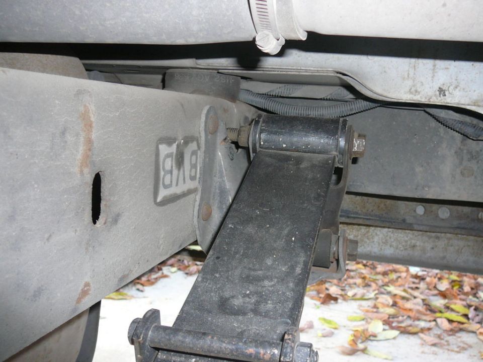 Leaf spring shackle and 'BXB' frame bracket under a truck, rusty boxed frame rail