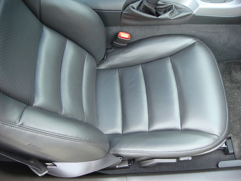 Close-up of a perforated leather car seat with a seatbelt and part of the gear shifter visible