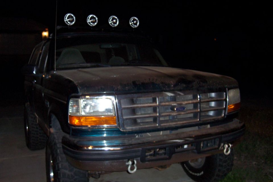 Dark green Ford Bronco front view with four lights on roof rack. Grille is chrome