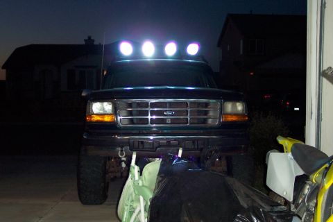 1995 Ford Bronco - The front of a dark-colored Ford Bronco is visible, equipped with a light bar and parked near a garage.