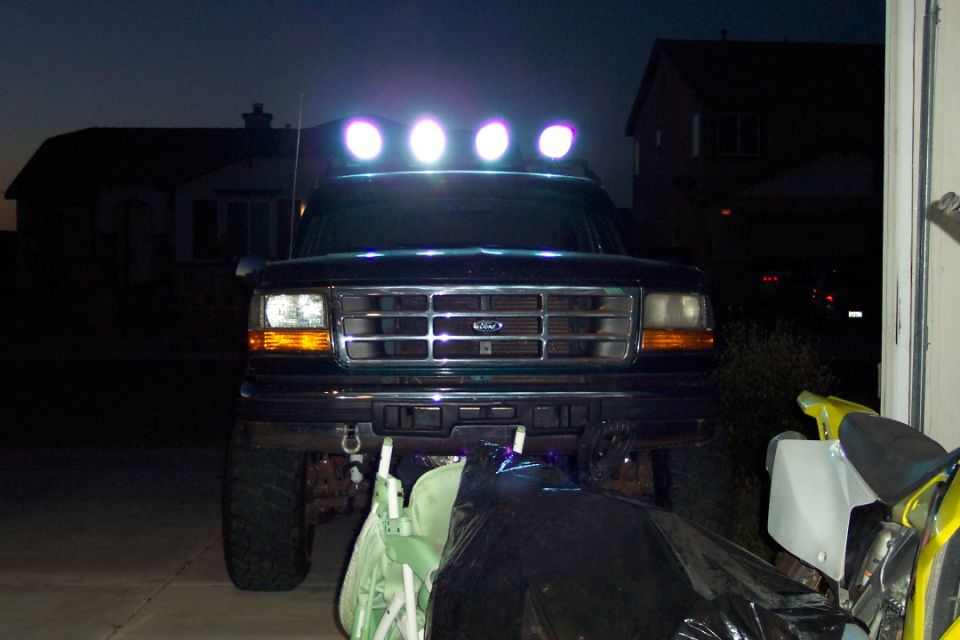 Front view of a 1995 Ford Bronco with a light bar on top, parked in a driveway at dusk