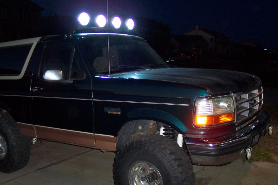 Dark green Ford Bronco with tan trim and a light bar on the roof, viewed from the front 3/4 angle