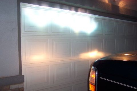 1995 Ford Bronco - Headlights shine brightly on a white garage door, with the front corner of a dark vehicle visible on the right.