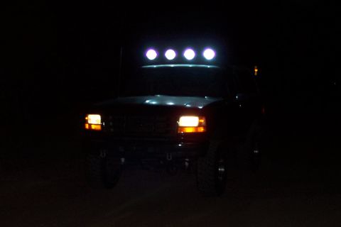 1995 Ford Bronco - A truck with a light bar on top is parked at night, with its headlights and roof lights on.