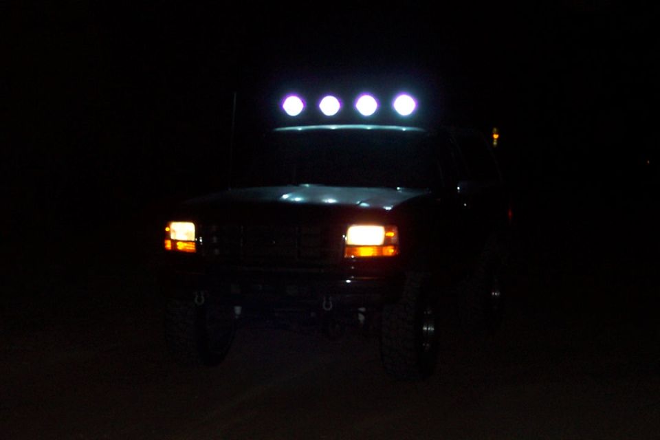 Front view of a dark-colored truck at night with four lights on the roof rack illuminated