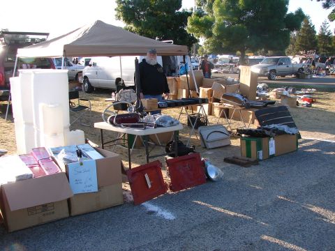 1973 Ford Ranchero - A variety of car parts are displayed on tables and on the ground at an outdoor swap meet, with vehicles visible in the background.