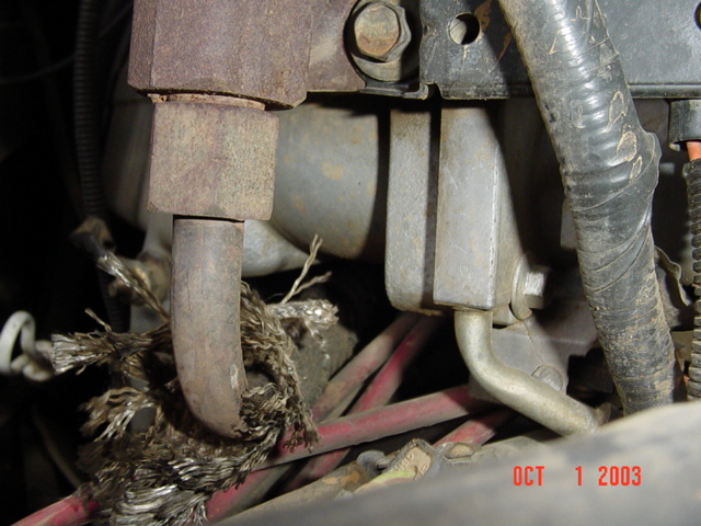 Frayed corroded under-hood cable and brake lines beside metal brackets and a rubber hose