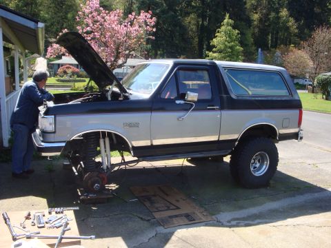 1989 Ford Bronco - A person works on the front end of a lifted Ford Bronco with its hood open.