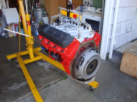 1989 Ford Bronco - A red engine with a clutch assembly is suspended from a yellow engine hoist, likely for installation or repair.
