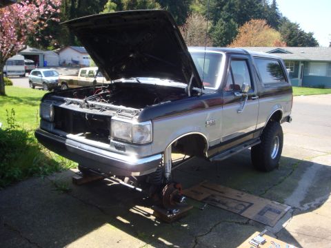 1989 Ford Bronco - Ford Bronco undergoing front-end maintenance with the hood up and wheels off.