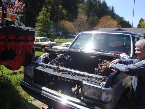 1989 Ford Bronco - A man works on the engine of a Ford truck while another engine is being lowered into place.