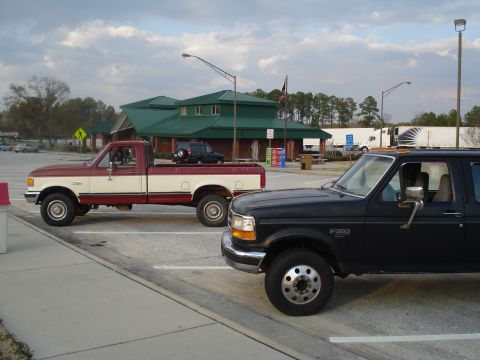 1989 Ford F-250 - A black 1989 Ford F-250 crew cab pickup truck is parked next to a red and white pickup truck at a rest stop.